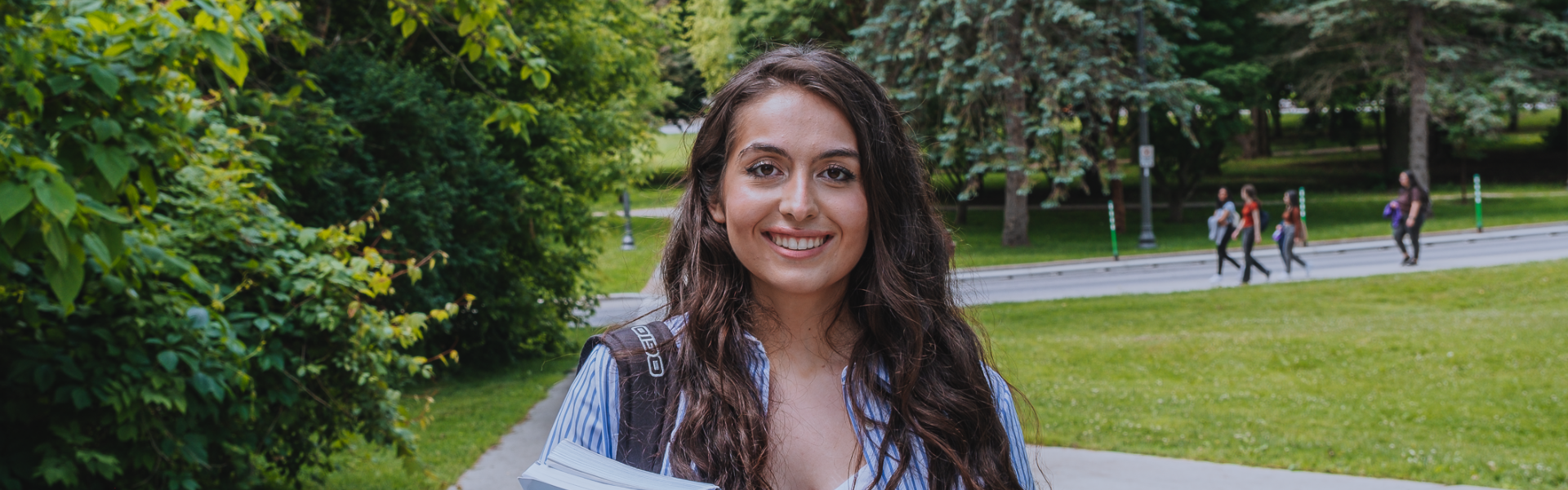 Young woman stands with books and a school backpack on a path.