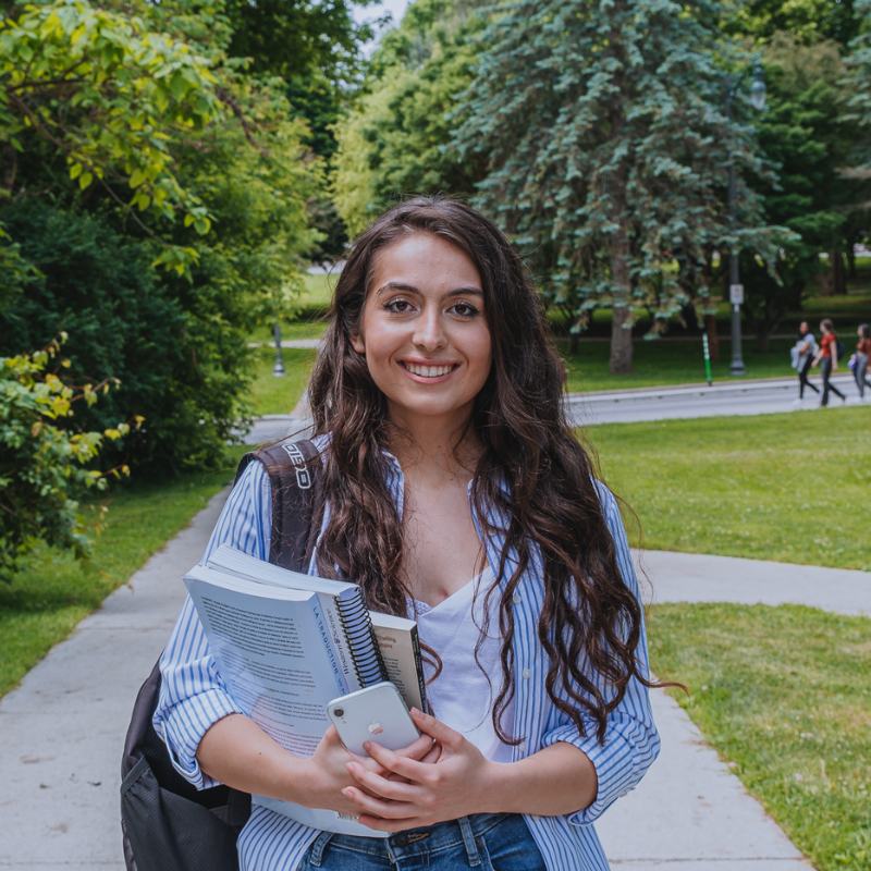 Young woman stands with books and a school backpack on a path.
